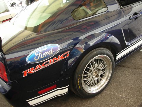 1998 Ford Crown Victoria - rear quarter of a dark blue Mustang shows a Ford Racing decal above a polished racing wheel and slick tire.