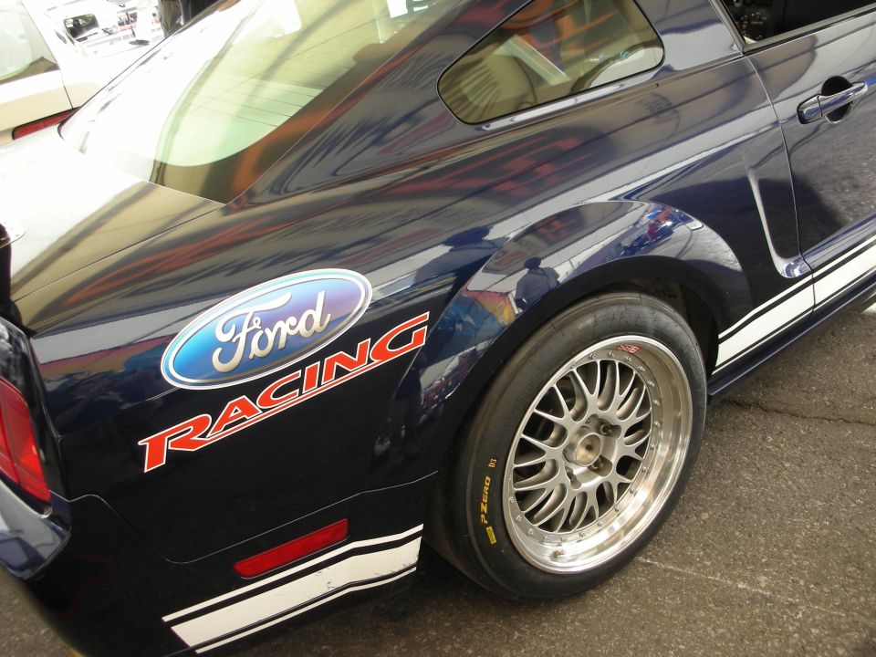 Rear quarter panel of a dark blue Mustang with Ford Racing decal and polished racing wheel