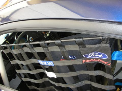 1998 Ford Crown Victoria - black driver-side window net with Ford Racing and Sparco logos hangs in the door opening of a caged race car.