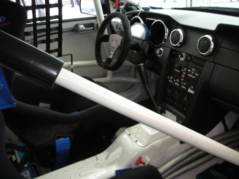 1998 Ford Crown Victoria - stripped race-car interior shows a roll cage, racing seat, dished steering wheel and white-painted floor pan.