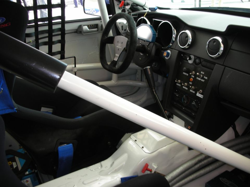 Stripped race-car interior with roll cage, racing seat and steering wheel, white painted floor