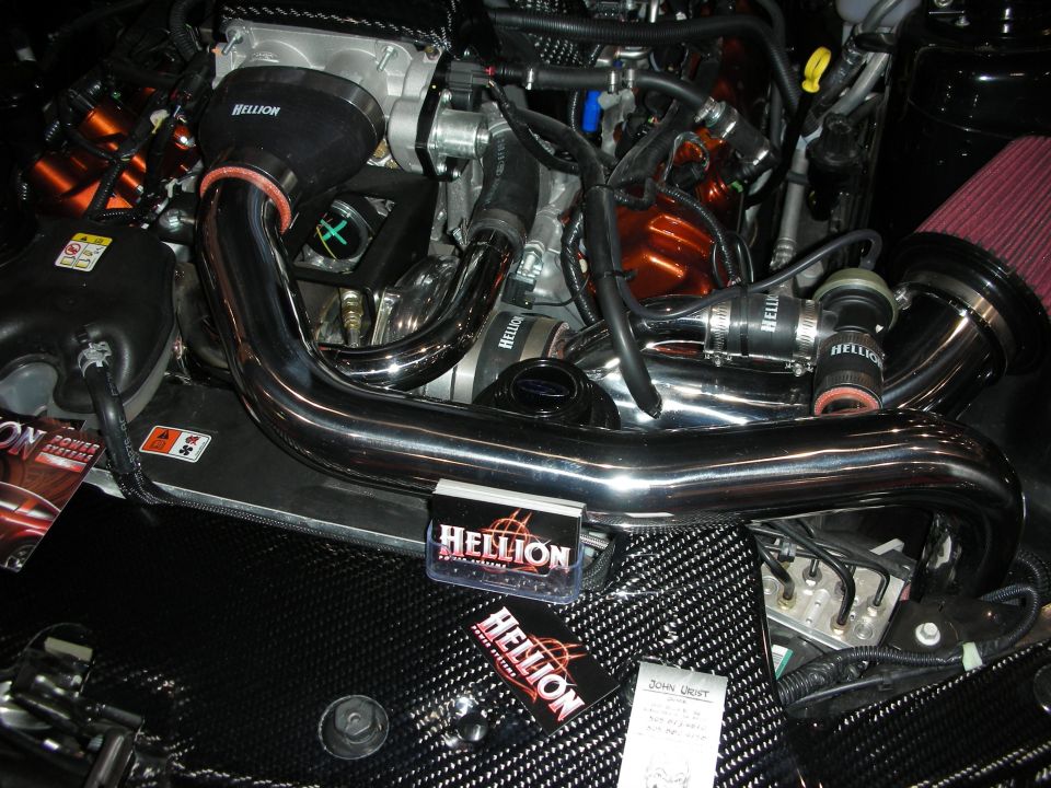 Engine bay with polished intercooler piping and Hellion-branded turbo plumbing on carbon panel