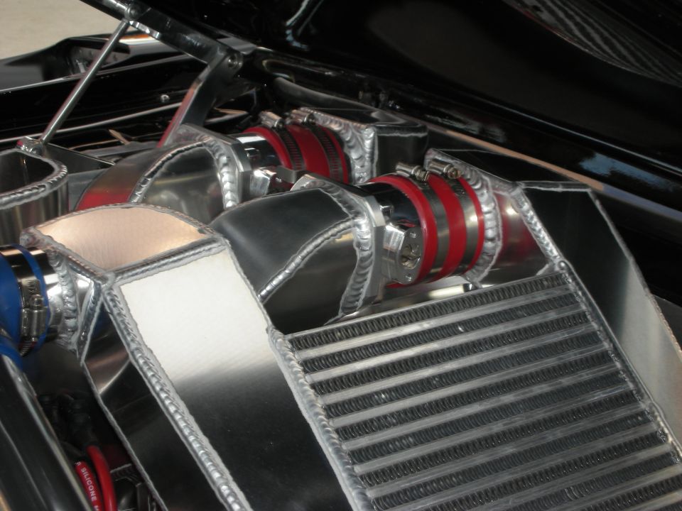 Polished aluminum intercooler and intake plumbing with red silicone couplers in a black bay