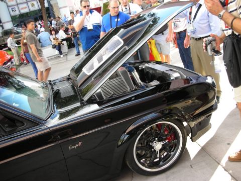 1998 Ford Crown Victoria - Side view of a lowered black custom car with raised hood revealing an intercooler, riding on chrome wheels with a red brake caliper, surrou…
