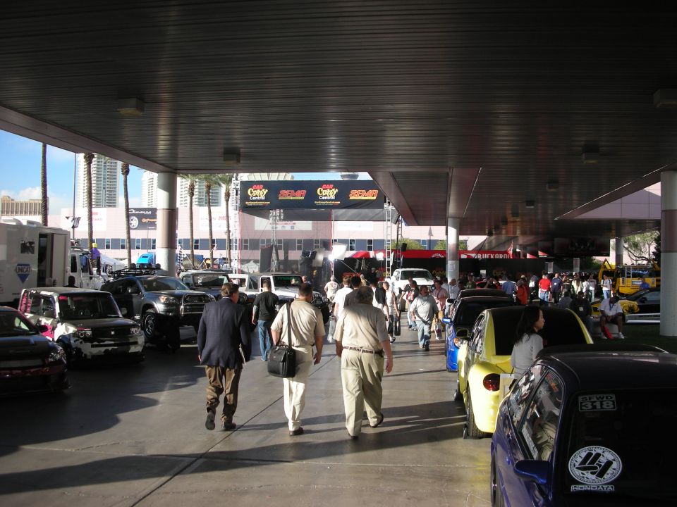 Crowd walking under a covered outdoor venue lined with show vehicles