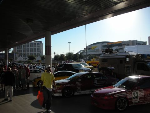 1998 Ford Crown Victoria - Sponsor-decaled race coupes, including a red car numbered 33, displayed under a covered concourse as a man in a yellow shirt walks past.