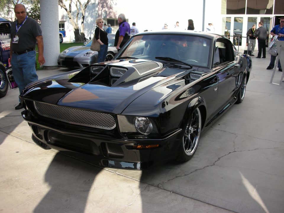 Black custom fastback with hood scoops and mesh grille parked at show