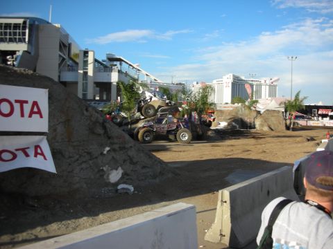 1998 Ford Crown Victoria - Tube-frame rock buggy crawling over a steep dirt mound on an outdoor demo course lined with Toyota banners, watched by a capped spectator.