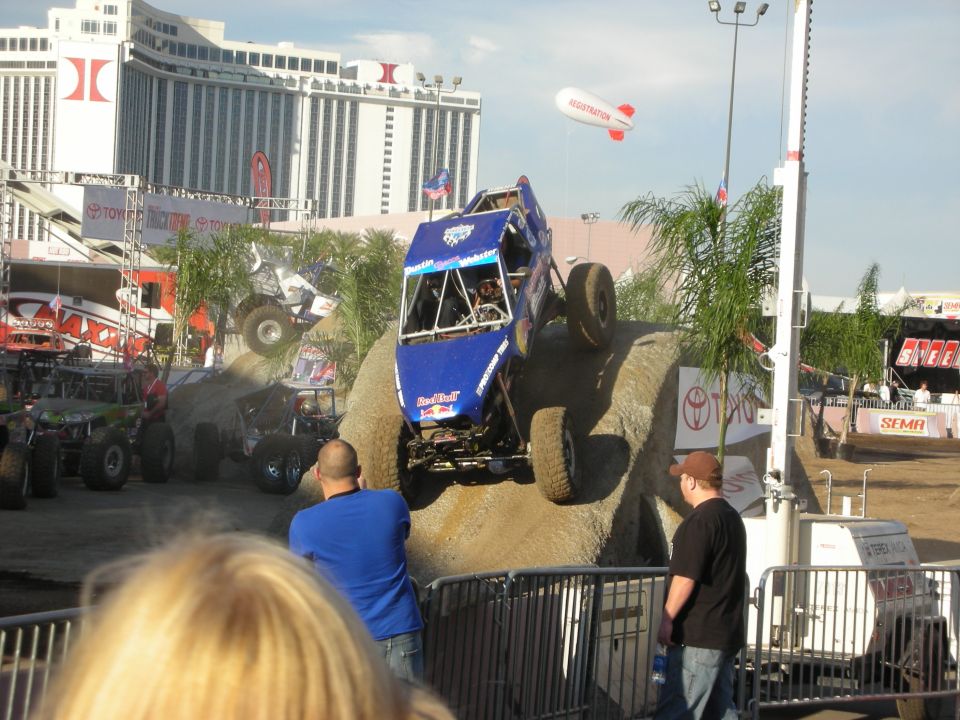 Blue tube-frame buggy catching air over a dirt jump with casino backdrop