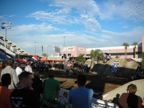 1998 Ford Crown Victoria - Crowd of spectators watches tube-frame buggies run an outdoor dirt obstacle course beneath SEMA signage and a bright blue sky.