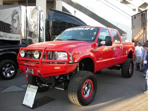 1998 Ford Crown Victoria - red lifted Ford Super Duty crew-cab pickup with a brush guard and Superlift banner sits on a black platform at a show.