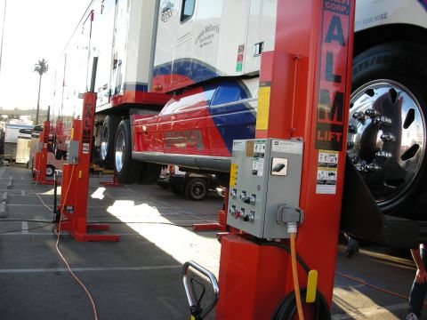 1998 Ford Crown Victoria - red, white and blue semi tractor is lifted on red ALM mobile column lifts during an outdoor demonstration.