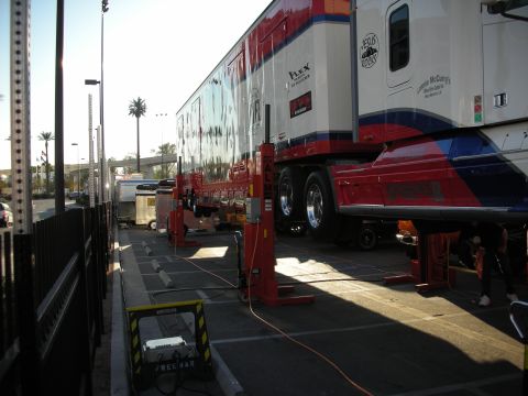 1998 Ford Crown Victoria - long red, white and blue semi truck and trailer is raised on a row of red column lifts in a paved outdoor lot.
