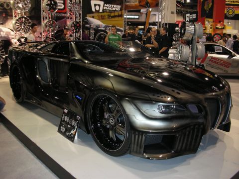 1998 Ford Crown Victoria - black custom concept sports car with heavily sculpted bodywork sits on display near Motegi Racing wheel signage indoors.