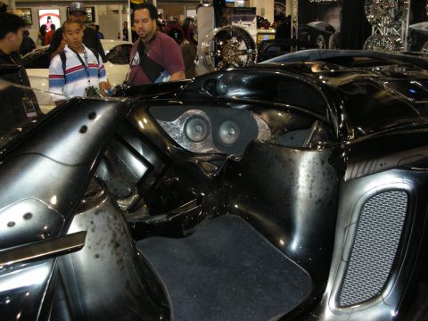 1998 Ford Crown Victoria - close-up of a black custom car shows its sculpted center tunnel and twin round gauges as onlookers stand behind it.