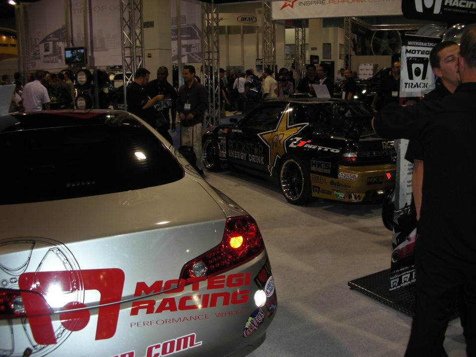 Show floor with a silver sedan and a gold Rockstar-liveried drift car beyond