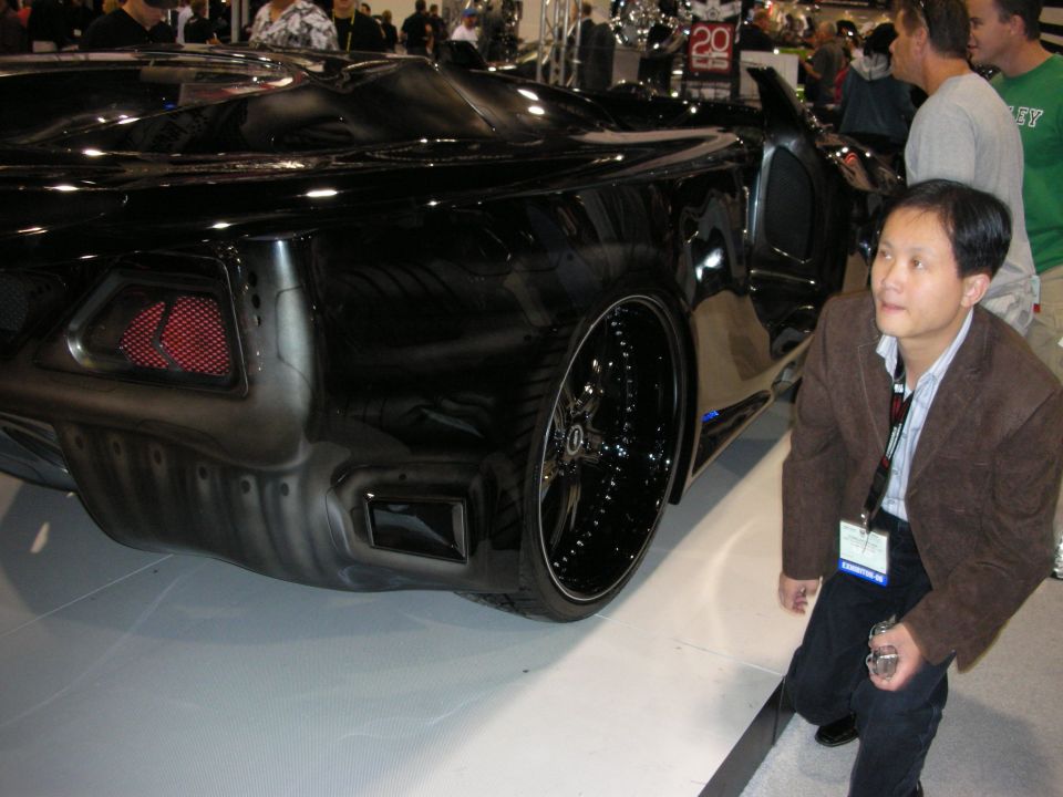 Rear of a black custom concept car on big black wheels as a man looks on