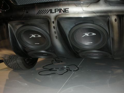 1998 Ford Crown Victoria - Two Alpine Type-X subwoofers sit in a molded enclosure beneath a vehicle, with wiring and a tire visible alongside.