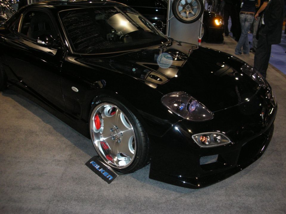 Black Mazda RX-7 sports car with chrome wheels on an indoor show floor