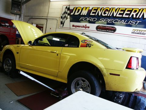 2001 Mercury Grand Marquis - Yellow Ford Mustang undergoing service in a garage with a JDM Engineering banner overhead.