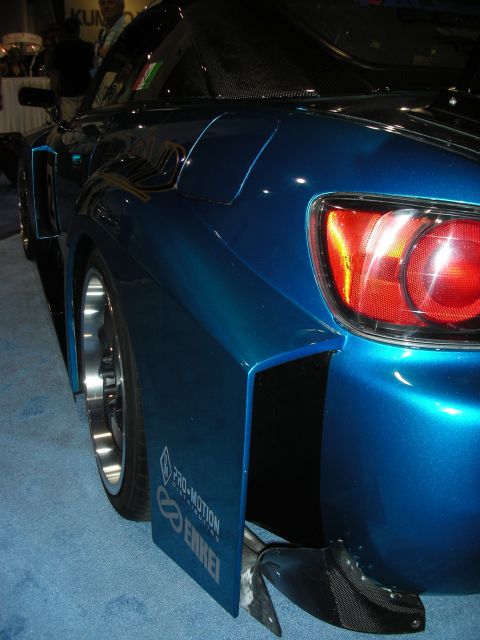 1998 Ford Crown Victoria - blue metallic rear quarter of a sports car shows a round taillight, polished wheel and Pro-Motion Enkei mud flap indoors.