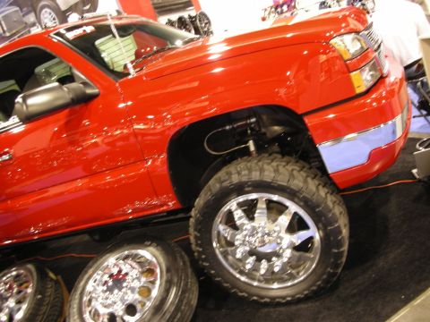 1998 Ford Crown Victoria - red Chevrolet Silverado pickup sits lifted on a display stand with a chrome wheel and off-road tire, spare wheels below.