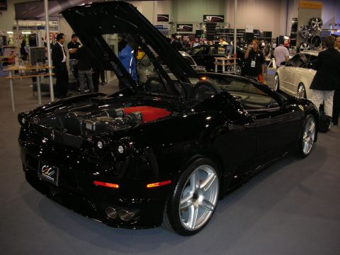 1998 Ford Crown Victoria - black Ferrari F430 Spider with its engine cover and roof open sits on a carpeted indoor show floor among other cars.