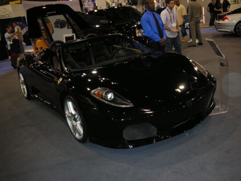 1998 Ford Crown Victoria - black Ferrari F430 Spider convertible sits on a blue carpet at an indoor show as two men stand beside it.
