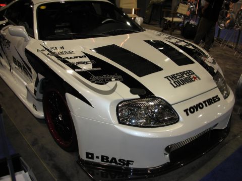 1998 Ford Crown Victoria - white Toyota Supra sport coupe with black racing graphics and Toyo Tires and BASF sponsor decals on display at an indoor show.