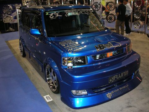 1998 Ford Crown Victoria - blue lowered Scion xB box-shaped wagon with custom wheels and sponsor decals on display at an indoor car show.