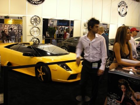 1998 Ford Crown Victoria - yellow Lamborghini Murcielago roadster on display at an indoor show with a wheel wall and people standing nearby.