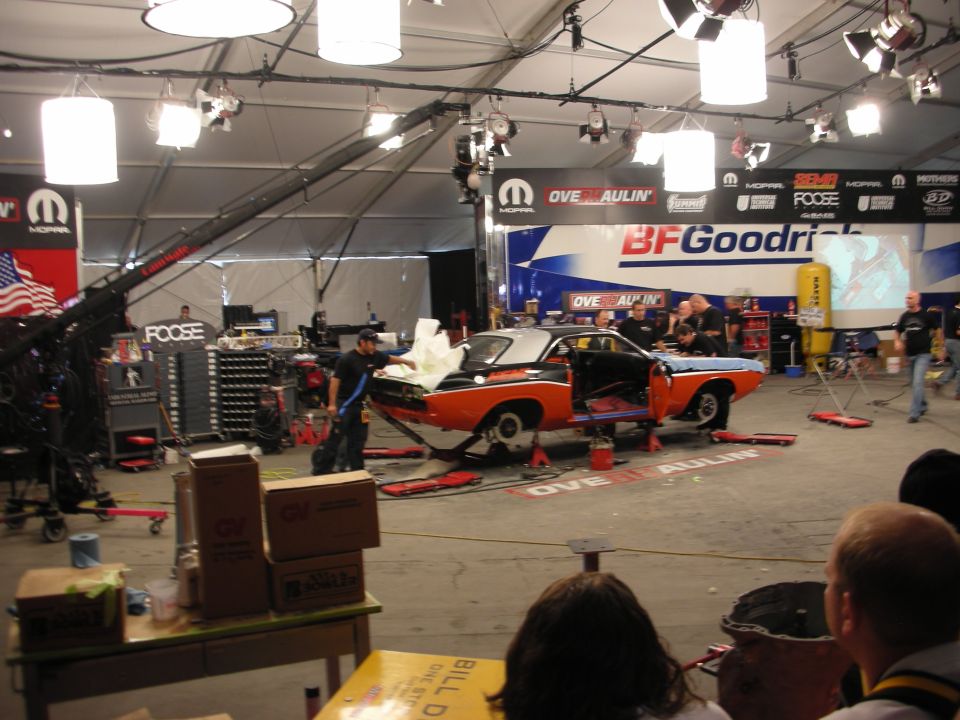 Orange muscle car on stands under stage lights at Overhaulin tent