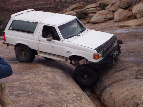 1993 Ford Bronco - A white 1993 Ford Bronco is shown off-roading over large rocks in a desert landscape.