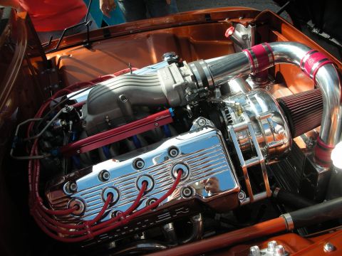 1998 Ford Crown Victoria - polished supercharged engine with chrome valve covers and red spark plug wires sits in an orange-painted engine bay.