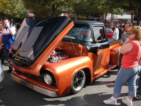 1998 Ford Crown Victoria - orange and black customized classic pickup truck with its hood open showing a chrome engine, with spectators outdoors.