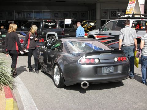 1998 Ford Crown Victoria - Rear three-quarter view of a gray Toyota Supra with rear spoiler and large exhaust tip among other cars and people outdoors.