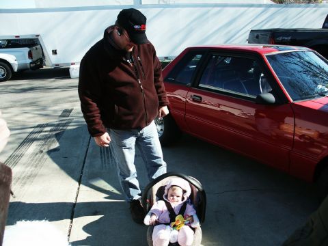 2001 Mercury Grand Marquis - A red coupe with a racing roll cage is parked outdoors next to a man and a baby in a car seat.