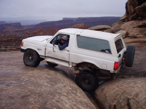 1993 Ford Bronco - White 1993 Ford Bronco is shown off-roading through a rocky canyon landscape.
