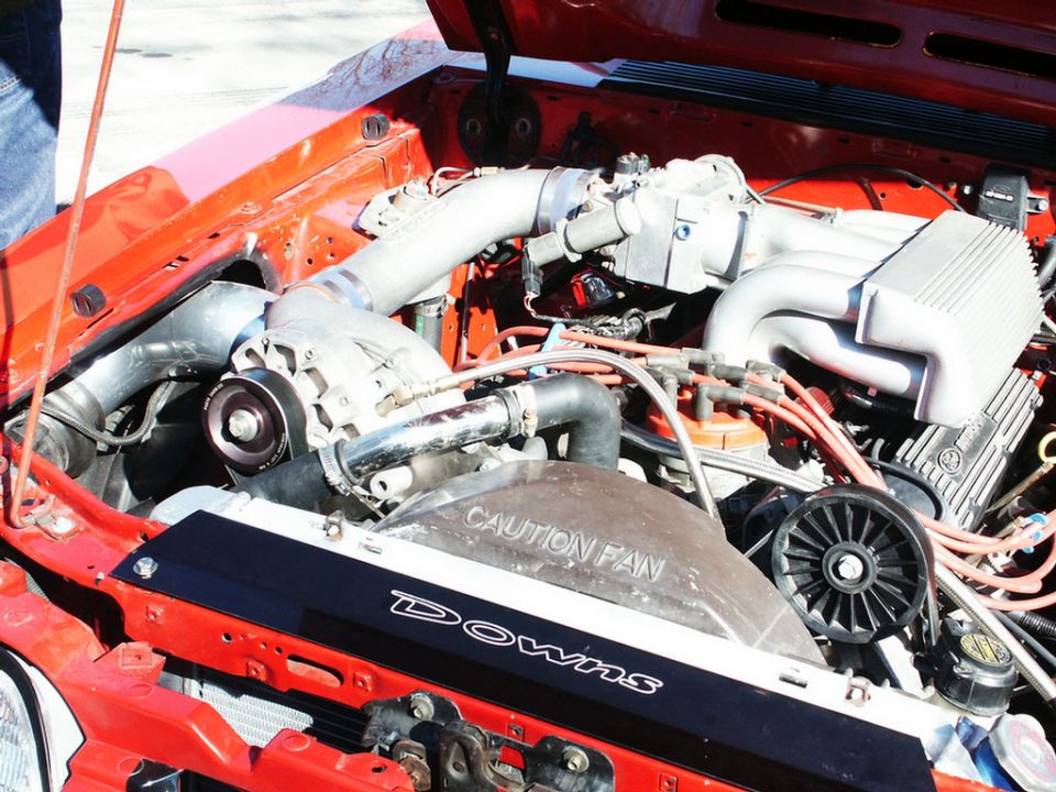 Engine bay with a supercharger, intake manifold, and fan shroud with 'Downs' and 'CAUTION FAN' text