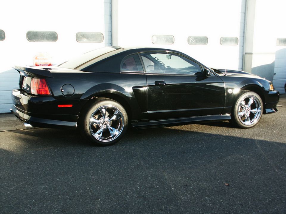 Black coupe with chrome wheels parked in front of a garage door