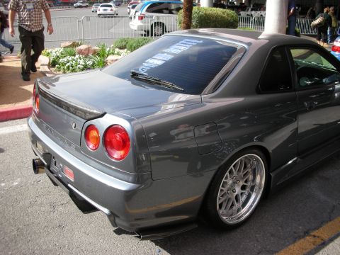1998 Ford Crown Victoria - Rear three-quarter view of a gray Nissan Skyline R34 coupe with round taillights and silver mesh wheels in a parking area.