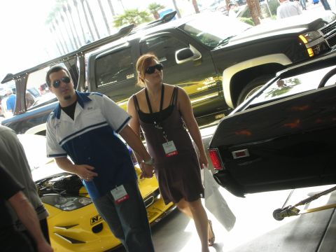 1998 Ford Crown Victoria - man and woman in sunglasses walk past a black SUV with roof rack and a yellow car under an indoor show tent.