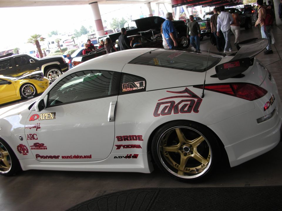 White Nissan 350Z coupe side profile with gold wheels and large rear wing at car show