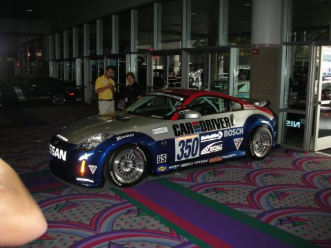 1998 Ford Crown Victoria - blue and silver Nissan 350Z race car wearing number 350 and Car and Driver and Bosch livery sits on patterned carpet at a show.