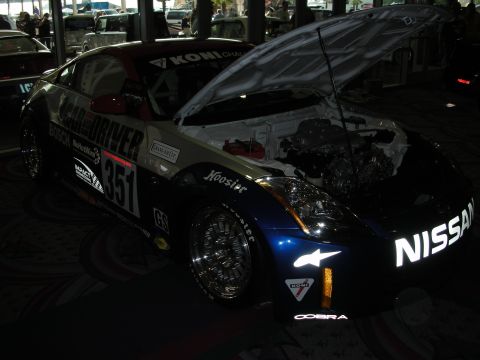 1998 Ford Crown Victoria - dark Nissan 350Z race car numbered 351 sits with its hood open exposing the engine, wearing Bosch and Koni decals at a show.