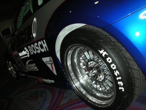 1998 Ford Crown Victoria - close-up shows a blue race car's polished multi-spoke wheel wrapped in a Hoosier tire, with Bosch and Koni decals on the bodywork.