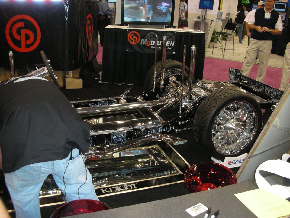 Chromed custom car chassis with hydraulic rams on display at trade show booth