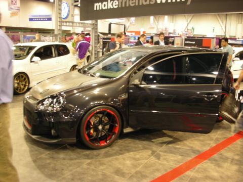 1998 Ford Crown Victoria - black Volkswagen Golf GTI hatchback with two-tone red and black wheels and an open door sits on display at an indoor show.