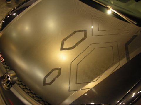 1998 Ford Crown Victoria - close-up shows a brushed metallic car panel etched with hexagonal geometric line patterns under warm lighting.