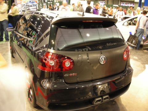 1998 Ford Crown Victoria - rear of a black Volkswagen Golf GTI shows carbon-fiber accents and red taillights amid a crowd at an indoor show.